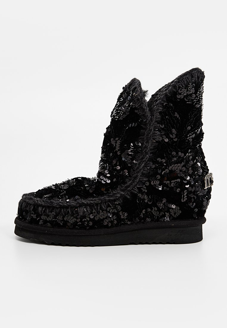Stivale alla caviglia nero con paillettes, punta arrotondata, texture morbida e spessa suola. Caratterizzato da cuciture decorative e un piccolo logo metallico.