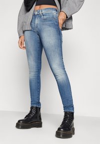 Jeans de mezclilla azul ajustados con detalles deslavados, diseño de cinco bolsillos y cierre de botón metálico, combinados con botas de plataforma negras con cordones.