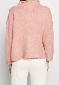 Stickad tröja i mjuk rosa med gula fläckar, hög krage och nedfallna axlar, med ribbad mudd och lös passform.