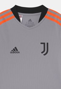 Harmaa urheilupaita mustalla kauluksella, oranssit olkapäällystykset, Adidas-logo vasemmalla ja Juventuksen jalkapalloseuran emblem oikeassa rinnassa.