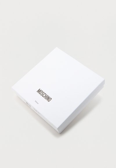 Λευκό τετράγωνο κουτί με την επιγραφή "MOSCHINO" και "Milano" με μαύρα γράμματα στο κέντρο του επάνω μέρους, μπροστά σε λευκό απλό φόντο.