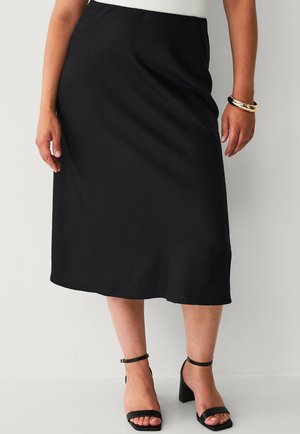 Zwarte midi-rok met een gladde textuur, gekenmerkt door een eenvoudig ontwerp en een lichte glans. Gecombineerd met zwarte hakken met enkelbandje.