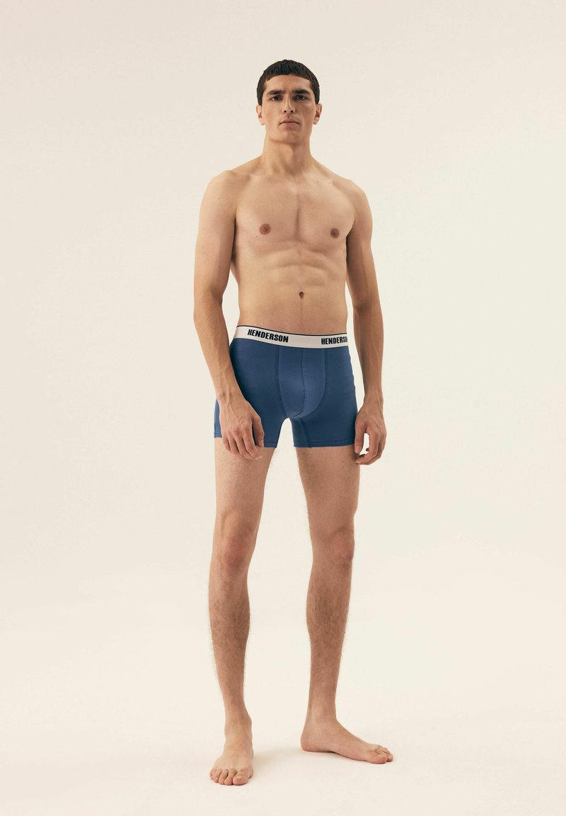 Męskie niebieskie bokserki z białą gumką z logo "Henderson". Gładki materiał, dopasowany krój i krótka długość nogawki.