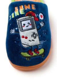 Chausson en peluche bleu mettant en avant un personnage de jeu vidéo en bande dessinée sur une planche à roulettes, avec des accents rouges et du texte brodé "GAME". Semelle extérieure beige.