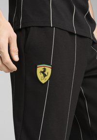 Fekete sportnadrág fehér csíkokkal, sárga Ferrari logóval a hátsó zsebben. Puha pamut anyag.
