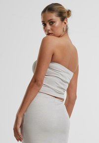 Haut tube ajusté gris clair en tissu texturé et scintillant, vu de côté, associé à une jupe assortie, présentant une silhouette élégante.