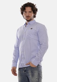 Camisa de manga larga azul claro hecha de algodón, con botón en el frente, un bolsillo en el pecho y un pequeño logotipo bordado en el lado izquierdo.