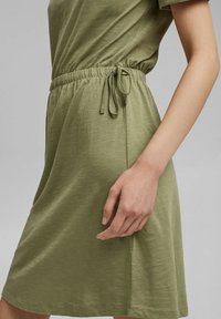 Robe vert kaki avec une coupe décontractée, des manches courtes et une taille élastique munie d'un cordon de serrage. Fabriquée en un tissu doux et texturé.