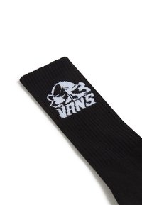 Schwarze Baumwollsocke mit gerippter Textur und weißem Vans-Logo, das in den Stoff eingestrickt ist, schräg zur besseren Sichtbarkeit.