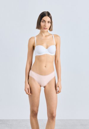 Soutien-gorge blanc rembourré avec bretelles réglables ; culotte rose pâle bordée de dentelle. Texture de tissu lisse, design sans coutures. Le mannequin pose devant un fond clair.