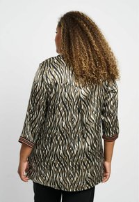 Seidenbluse mit einem mehrfarbigen wellenförmigen Muster in Brauntönen, Schwarz und Creme; verfügt über dreiviertellange Ärmel mit gestreiften Bündchen.
