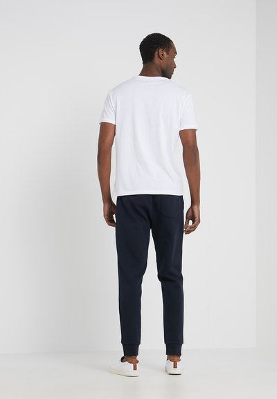 T-shirt en coton blanc associé à un jogging bleu marine avec des poignets côtelés, des poches avant et des baskets blanches avec des accents marron.