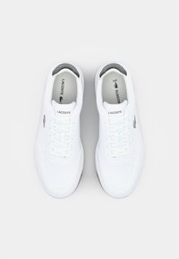 Baltos odinės sportinės bateliai su lygiu paviršiumi, turintys šešis skylučių užrišimui, toniniu siuvimu, pilku pamušalu ir mažą metalinį logotipą.