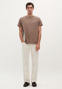 Bruine katoenen T-shirt met ronde hals, gecombineerd met crème-kleurige rechte broek en donkerbruine veterschoenen.