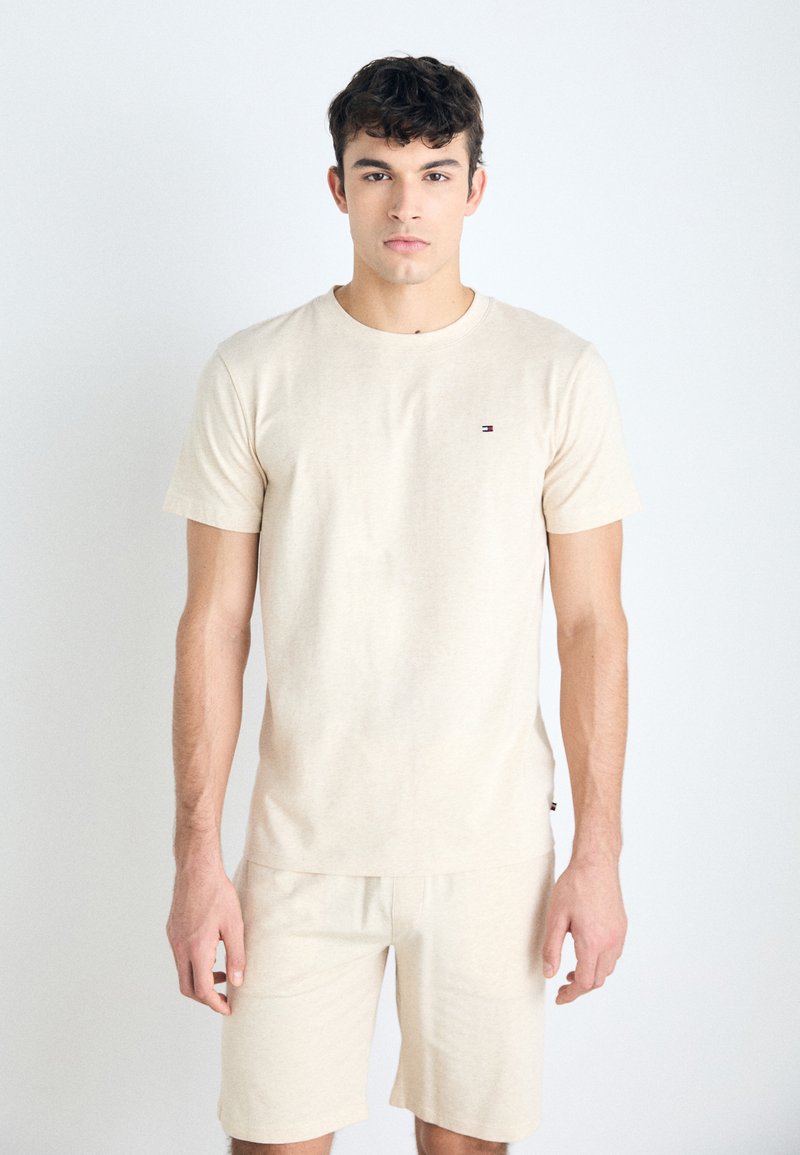 Camiseta de algodón beige con mangas cortas, escote redondo y pequeño logo bordado. Combinada con pantalones cortos beige a juego. Textura suave.