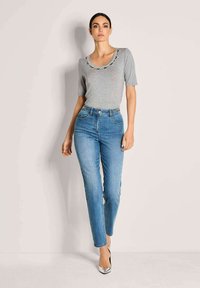 Grijze top met korte mouwen en geborduurd decolleté, gecombineerd met hoge spijkerbroek in blauw en zilveren hoge hakken.