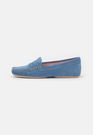Mocassins en suede bleu clair avec un détail de couture et un bout arrondi, dotés d'une semelle en caoutchouc beige. Design minimaliste avec une texture lisse.