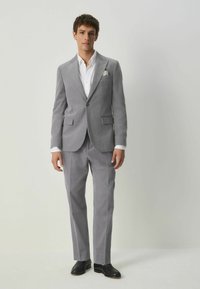 Grå kostym med enblads blazer, skräddarsydd passform och slät textur. Inkluderar en vit skjorta och svarta loafer-skor. Märkbar fickkvadrat.