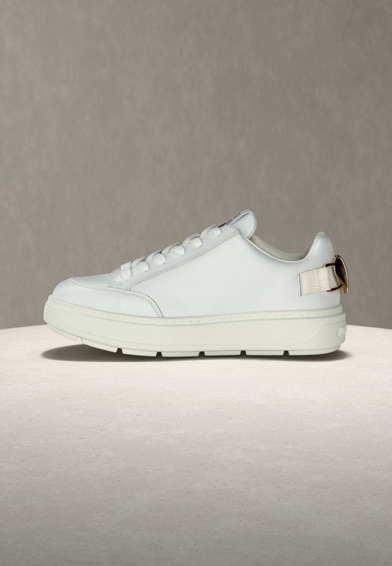 Λευκό χαμηλό αθλητικό παπούτσι με χοντρή σόλα, μπροστινό δέσιμο με κορδόνια και χρυσή αγκ ράφα στο πίσω μέρος, τοποθετημένο σε ουδέτερη επιφάνεια.