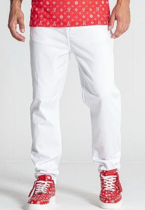 Pantalones de mezclilla blanca con corte recto y costuras visibles. Combinados con zapatillas rojas con patrón que tienen cordones blancos y suelas de goma.