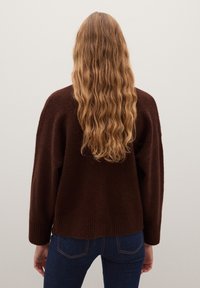 Brauner, übergroßer Pullover aus einem strukturierten, flauschigen Material. Verfügt über gerippte Bündchen und Saum. Modell ist von hinten zu sehen, Haare fallen hinab.