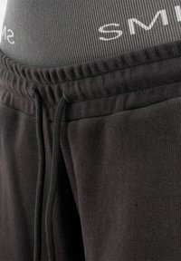 Zbliżenie na czarne spodnie dresowe z polaru z elastycznym pasem i czarnymi sznurkami na szarych legginsach z częściowym białym napisem.