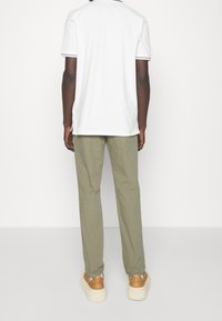 Biała koszulka polo z krótkim rękawem i czarnym wykończeniem, zestawiona z oliwkowozielonymi spodniami i beżowymi trampkami. Gładka tkanina o swobodnym kroju.