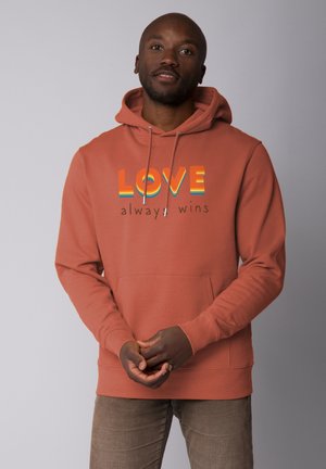 Rust-colored hoodie with kangaroo pocket, featuring the text “LOVE always wins” in multicolor font. Smooth cotton blend material.