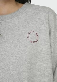 Grijze sweatshirt met een gestructureerde afwerking, voorzien van een ronde print met de tekst "CLASSIC AESTHICS" in bordeauxrood. Ronde halslijn, casual ontwerp.