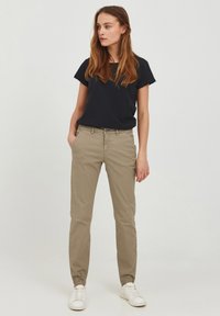 Chino beige chiaro con una vestibilità slim, caratterizzati da chiusura a bottone, passanti per la cintura e tasche laterali, abbinati a una t-shirt nera a girocollo e sneakers bianche.