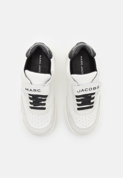 Witte leren sneakers met zwarte accenten, voorzien van een klittenbandsluiting, geperforeerde neus en een merklabel op de hiel. Klassiek laag model.