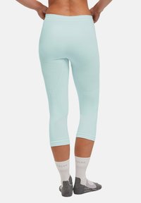 Mintgrüne Kompressionsleggings mit passgenauer Form, die strukturierte Einsätze und eine Länge bis zur Mitte der Waden aufweisen. Kombiniert mit grau-weißen Socken.