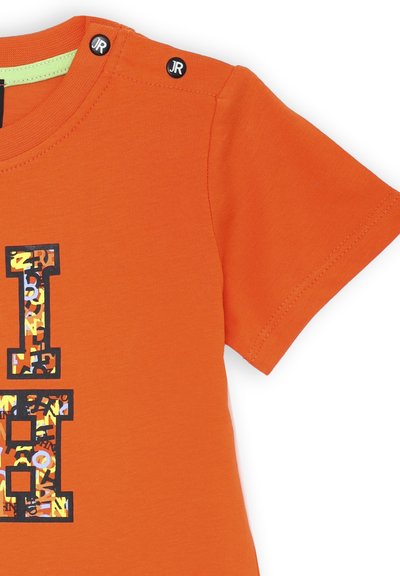 T-shirt di cotone arancione con maniche corte, caratterizzato da un motivo grafico colorato e due bottoni a pressione neri sulla spalla.
