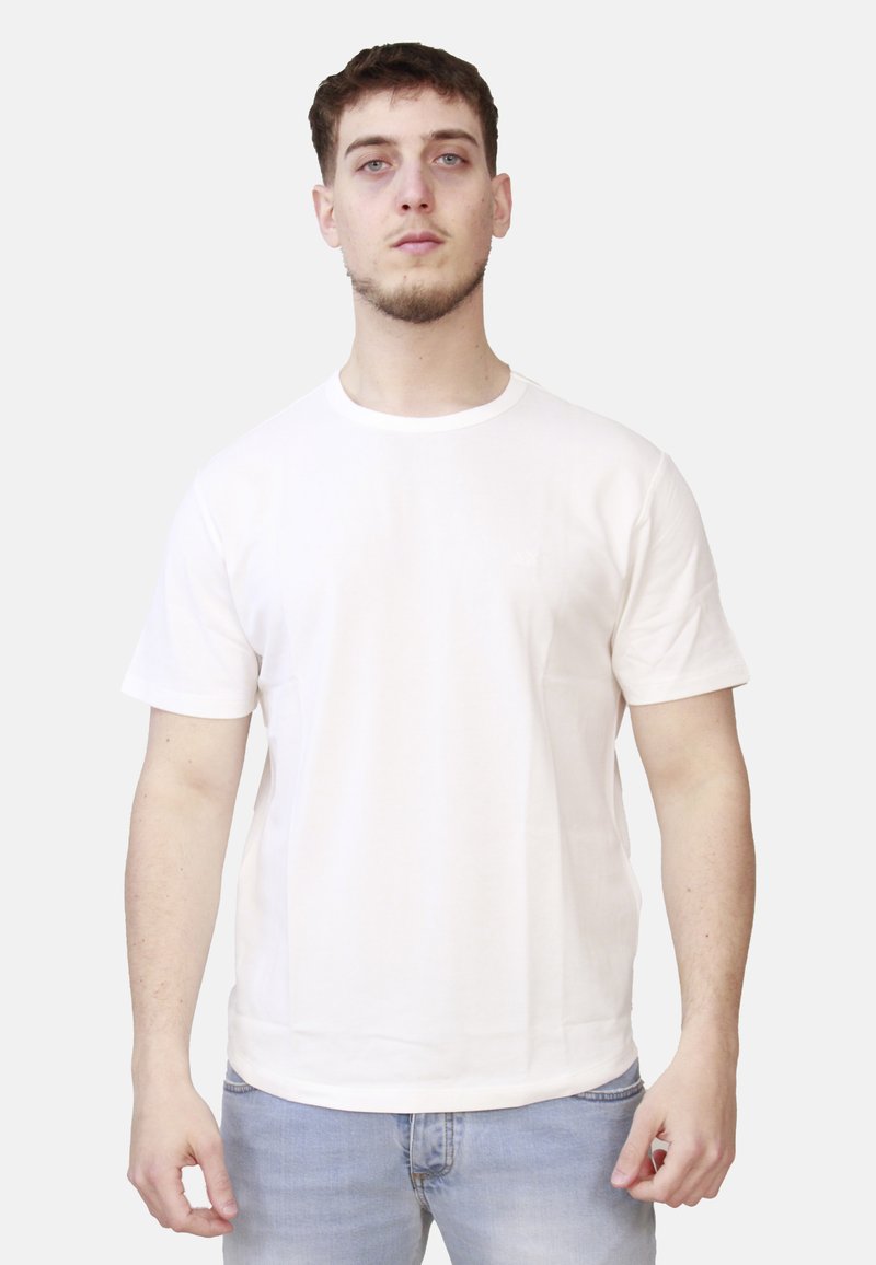 T-shirt in cotone beige chiaro con maniche corte, scollo rotondo e taglio dritto. Presenta un design minimalista e nessun logo visibile.