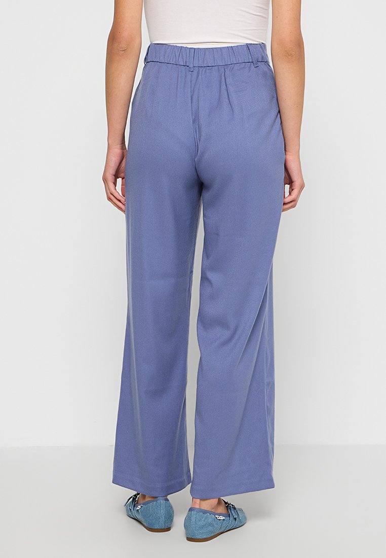 Jasnoniebieskie, szerokie spodnie z elastycznym paskiem, o gładkiej fakturze, bez widocznych wzorów i elementów metalowych.