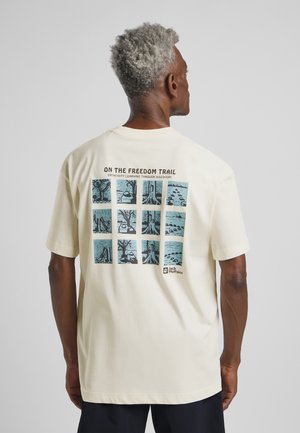 Cream-colored cotton t-shirt featuring a graphic print on the back with blue illustrations in a grid pattern; short sleeves, relaxed fit.