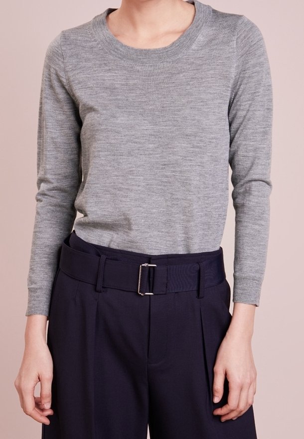 Une personne porte un pull gris ajusté à manches longues, rentré dans un pantalon bleu marine foncé taille haute avec une large ceinture et une boucle métallique rectangulaire.