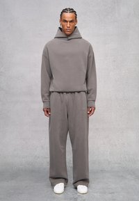 Grauer Kapuzenpullover mit lockerem Schnitt und langen Ärmeln, kombiniert mit passenden Jogginghosen mit elastischem Bund und Logodetails.