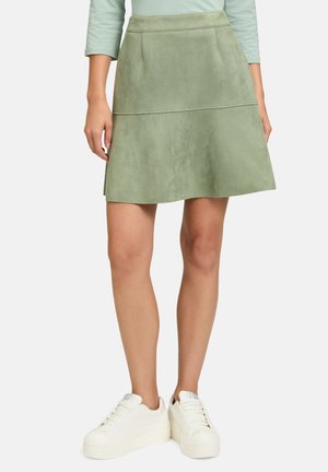Grüner Faux-Suede A-Linien-Rock mit glatter Oberfläche, zwei Vordertaschen und hoher Taille, kombiniert mit weißen Plateausneakern.