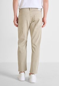 Pantalones de algodón beige con un diseño de pierna recta, que cuentan con bolsillos traseros y detalles cosidos, combinados con zapatillas blancas.