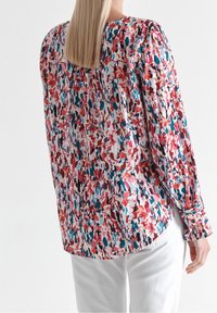 Blusa a maniche lunghe multicolore con motivo floreale, con scollo rotondo, spalle arricciate e orlo curvo. Realizzata in tessuto leggero.