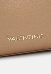 Bežna usnjena torbica z teksturirano površino in zlatim logotipom "Valentino", ki je jasno izpostavljen. Ima eleganten dizajn in nevtralno barvo.