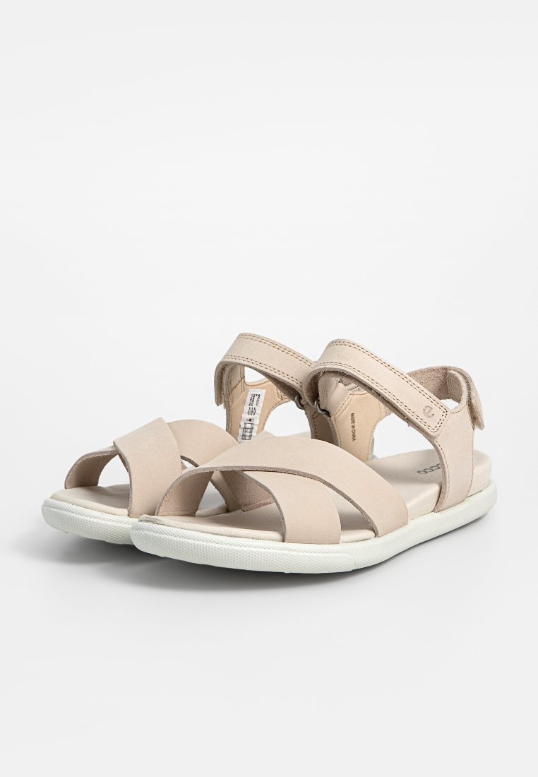 Beige Sandalen mit Kreuzriemen, aus weichem Wildledermaterial gefertigt. Verstellbarer Klettverschluss und eine weiße Gummisohle. Minimalistisches Design.