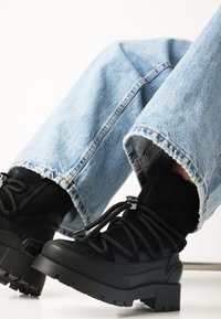 Černé šněrovací kotníkové boty s robustní podrážkou, vyrobené z nubuku a gumy. Slučují se s opotřebovanými světle modrými džíny.