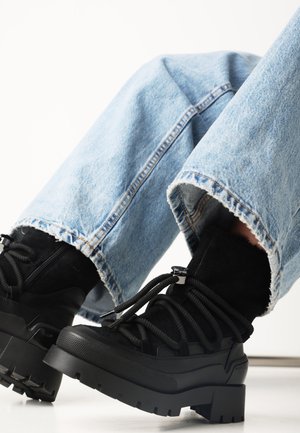 Czarne lace-up botki za kostkę z grubą podeszwą, wykonane z zamszu i gumy. Połączone z przetartymi jasnoniebieskimi dżinsami.