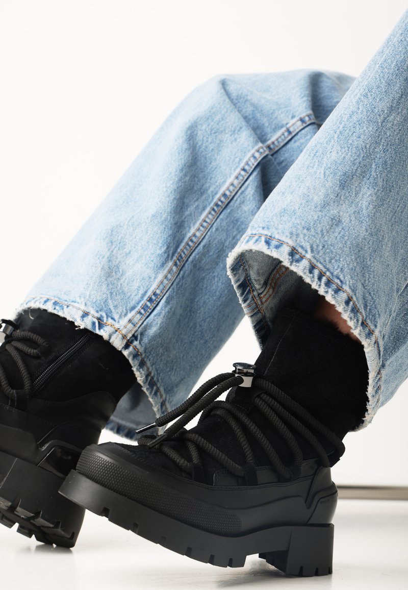 Černé šněrovací kotníkové boty s robustní podrážkou, vyrobené z nubuku a gumy. Slučují se s opotřebovanými světle modrými džíny.