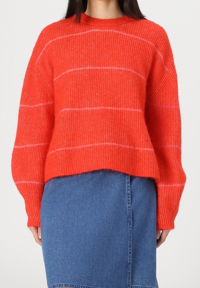 Punainen raidallinen neulepaita, jossa on rento istuvuus, ribattu tekstuuri ja pyöreä pääntie. Yhdistetty farkkuhameen kanssa kontrastiksi.