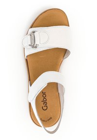 White leather sandal with a wide strap and decorative buckle. Cushioned brown insole and rubber sole feature a simple, practical design.