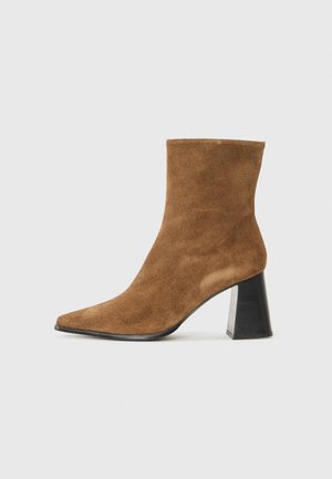 Bottine en daim marron avec un bout pointu et un large talon noir. Texture lisse et design minimaliste. Convient à diverses tenues.