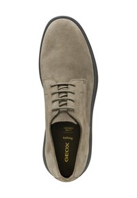 Zapato de gamuza beige con punta redonda, cinco ojetes, cordones planos y suela de goma negra texturizada. Logo dorado en la plantilla.